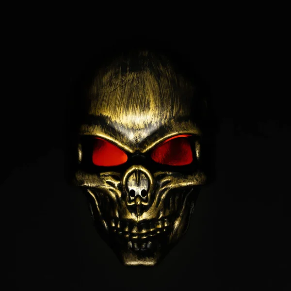 Golden skull with red eyes on black background.