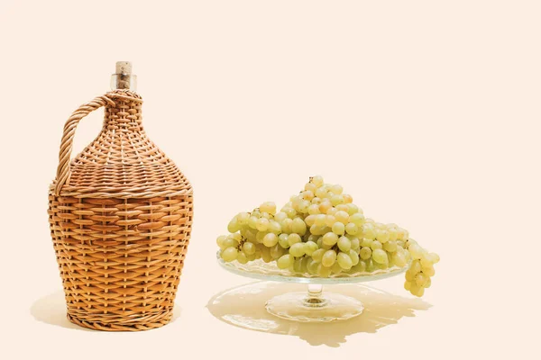 Aesthetic composition of green (white, Victoria) grapes and vintage braided wine bottle. Autumn harvest, vineyard concept.