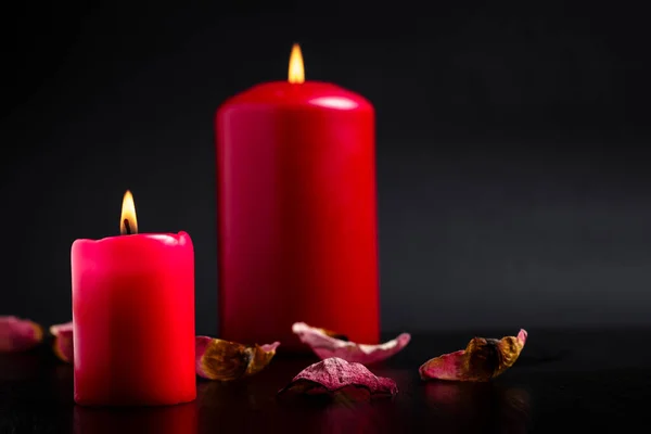 Romantic background. Red candles are burning strewn with rose petals on a black background