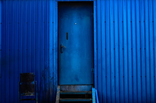 Blue metal wall. A blue metal door and a blue trash can next to it. background picture.