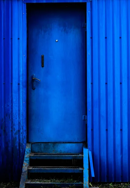 Blue metal wall. A blue metal door and a blue trash can next to it. background picture