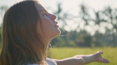 Hamile kadın yeşil çimlerle sahada duruyor ve ellerini kavuşturup dua ediyor. Güneş ışığı yaz titreşimleri