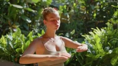 Hamile kadın arka planda bahçeyle yoga pozu verip karnını kucaklar. Güneş ışığı yaz titreşimleri