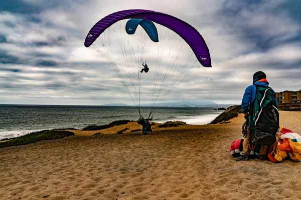 Sahilde dramatik bir sahne. Arka planda uğursuz bulutlar olan iki parafinacı insan.