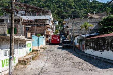 red truck stops in hillside brick street of rural Puerto Vallarta with homes and shops on both sides