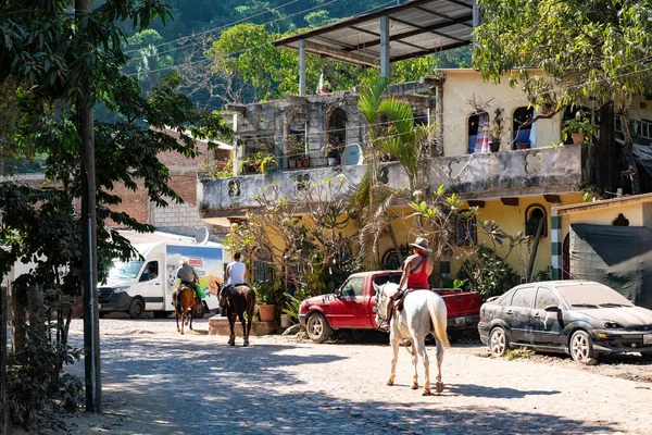 three people ride their horses on the rural streets of Puerto Vallarta