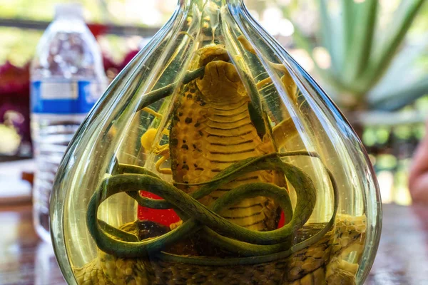 ornate and decorative bottle holding a hooded cobra coiled up inside surrounded by wine with water bottle in background