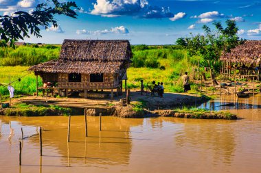 Bago, Myanmar - 02 Aralık 2012: Geleneksel Myanmar bambu kırsal evi ya da kırsal kesimde nehir ve uzun kuyruklu teknelerin bulunduğu cambaz ayaklıkları üzerindeki kulübe