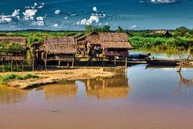 Bago, Myanmar - 02 Aralık 2012: Geleneksel Myanmar bambu kırsal evi ya da kırsal kesimde nehir ve uzun kuyruklu teknelerin bulunduğu cambaz ayaklıkları üzerindeki kulübe