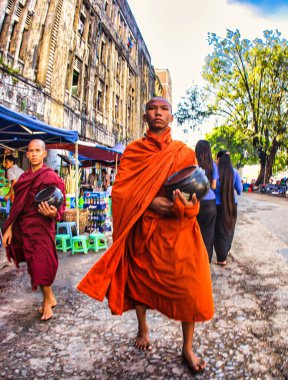 Yangon, Myanmar - 02 Aralık 2012: Bornozlu bir Budist keşiş, elinde sadaka kasesiyle caddenin kaldırımında yürüyor