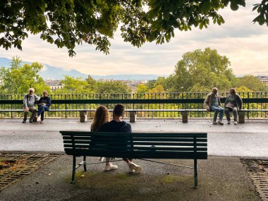 Cenevre, İsviçre - 15 Eylül 2021: Parktaki bankta oturan ve şehir manzaralı genç bir çiftin romantik görüntüsü