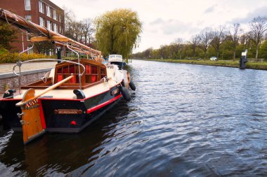 Voorburg, Hollanda - 04 Mayıs 2021: Nehir boyunca uzanan küçük bir köyün limanına tarihi bir ahşap tekne yanaştı.