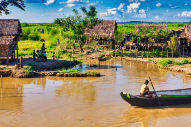 Bago, Myanmar - 02 Aralık 2012: Geleneksel Myanmar bambu kırsal evi ya da kırsal kesimde nehir ve uzun kuyruklu teknelerin bulunduğu cambaz ayaklıkları üzerindeki kulübe