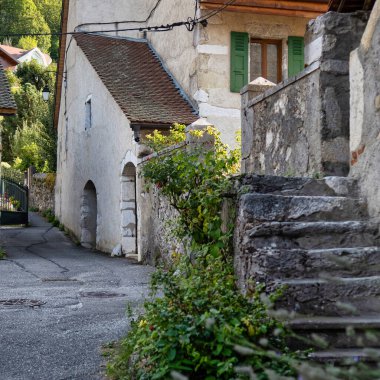 Menthon Aziz Bernard, Fransa - 10 Eylül 2020: Taşlı tarihi bir Fransız köyü manzarası, pencerelerin önündeki kepenkler ve yuvarlak kapılı kemerler