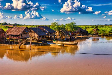 Bago, Myanmar - 02 Aralık 2012: Geleneksel Myanmar bambu kırsal evi ya da kırsal kesimde nehir ve uzun kuyruklu teknelerin bulunduğu cambaz ayaklıkları üzerindeki kulübe