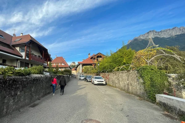 Menthon St. Bernard, Fransa - 02 Ekim 2021: İki Latin kadın eski Fransız dağlık evleri ve uzaktaki bir kaleyle çevrili küçük bir sokakta yürüyorlar.