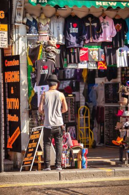 Londra, Birleşik Krallık - 18 Mart 2009: Renkli Camden yol pazarındaki hediyelik eşya dükkanının önünde şapka ve gömlek satan bir adam