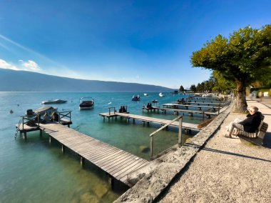 Menthon Saint Bernard, Fransa - 10 Ekim 2021: Yaşlı bir çift limana ve dağ gölüne bakan bir bankta dinleniyor ve oturuyor.