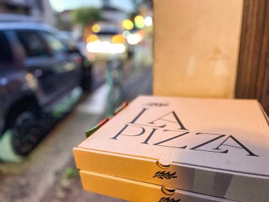 Menthon Saint Bernard, Fransa - 23 Ekim 2021: Geceleri şehir ışıkları altında dışarıda kahverengi bir pizza kutusu görülmektedir.