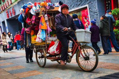 Chengdu, Çin - 29 Kasım 2009: Yaşlı bir vatandaş kaldırımda bisiklet sürerken mallarını satıyor ve taşıyor