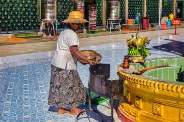 Yangon, Myanmar - 3 Aralık 2012: Geleneksel elbiseli, bambu şapkalı ve kilden maskeli bir kadın Yangon tapınağında hediye tepsisi hazırladı.