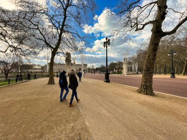 Londra, Birleşik Krallık - 6 Mart 2022: Buckingham Sarayı ve güzel Kraliçe Victoria Anıtı 'na giden ünlü alışveriş merkezinin ağaçlarının altında yürüyen insanlar