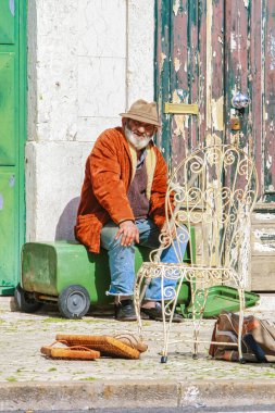Lizbon, Portekiz - 5 Mart 2008: Yaşlı bir vatandaş sokakta bir çöp konteynerinin üzerinde oturuyor
