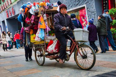 Chengdu, Çin - 29 Kasım 2009: Yaşlı bir vatandaş kaldırımda bisiklet sürerken mallarını satıyor ve taşıyor