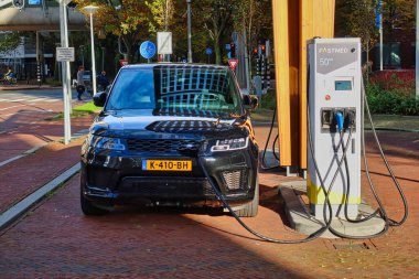 Den Haag, Hollanda - 03 Kasım 2021: bir elektrikli araba park halinde ve bir şehrin ofis bölgesinde bir kamu şarj istasyonunda şarj ediliyor