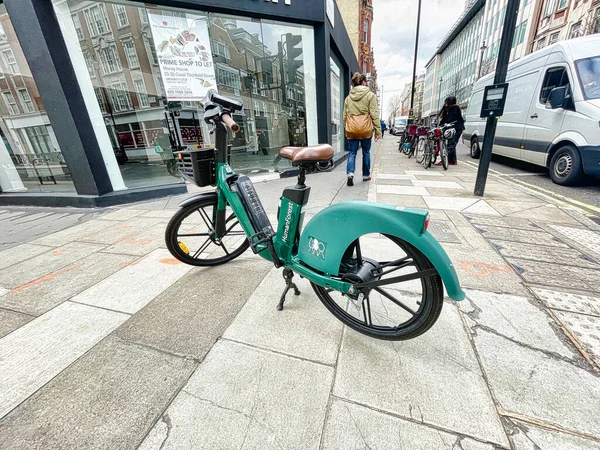 London, United Kingdom - March 07 2022: a green electric bicycle of a public share system has been left parked in the middle of a sidewalk