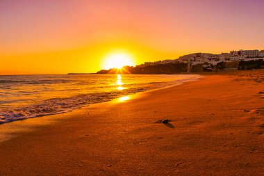 Albufeira, Portekiz - 18 Ocak 2016: Okyanus dalgaları gün batımında sahile vuruyor. Sahilde deniz kabukları görülür..