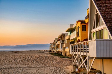 Oxnard, ABD - 21 Şubat 2020: Renkli ahşap kiralama mülkleri plajda dizilmiş, cennet gibi bir gün batımıyla