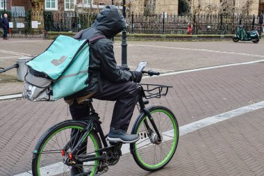 The Hague, Netherlands - January 03 2022: a food delivery person is standing on his bicycle checking the screen of his mobile phone for instructions