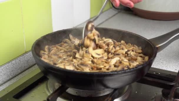 A gombát és a hagymát egy serpenyőben sütik a házi konyhában.. — Stock videók
