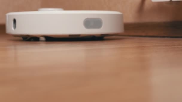 White Robotic Vacuum Cleaner удаляет обломки из ламината — стоковое видео