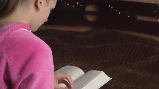 Молодая женщина в розовом пижаме читает книгу — стоковое видео