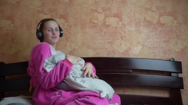Дівчина в піжамі на ліжку слухає музику через навушники та танці Slowmo — стокове відео