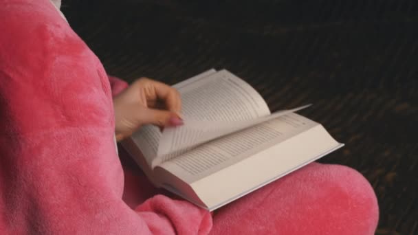 Νεαρή γυναίκα σε ροζ πιτζάμες κάθεται διαβάζει ένα βιβλίο — Αρχείο Βίντεο