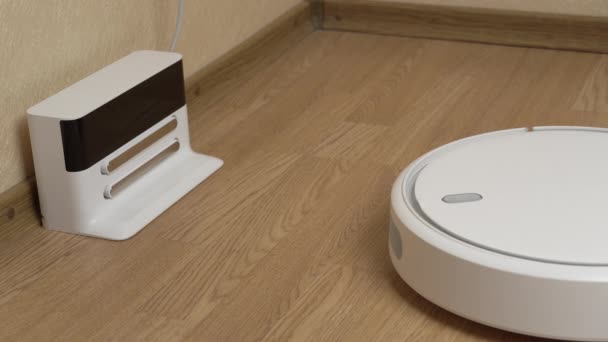 Белый роботизированный пылесос заканчивает очистку и приезжает к своей зарядной станции — стоковое видео