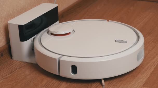 White Robotic Vacuum Cleaner Starts Cleaning From Its Charging Station — Stock Video