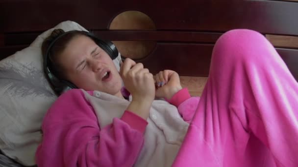 Girl in Pajamas on the Bed Listens to Music Through Headphones and Dances Slowmo — Stok Video