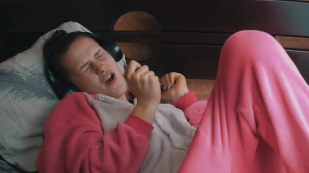 Dziewczyna w piżamie na łóżku słucha muzyki przez słuchawki i tańce Slowmo — Wideo stockowe