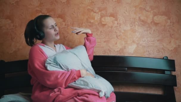 Mädchen im Schlafanzug auf dem Bett hört Musik über Kopfhörer und tanzt Slowmo — Stockvideo