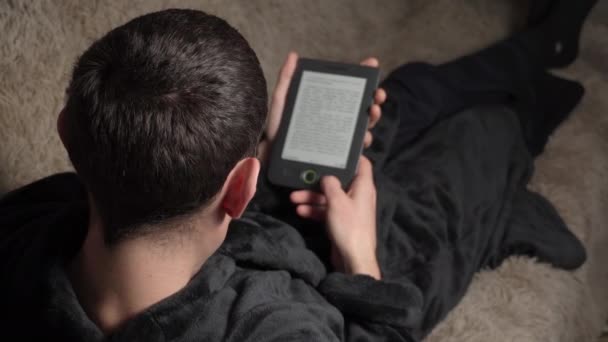 Man in een badjas leest een e-boek terwijl hij op de bank zit — Stockvideo