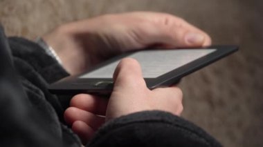 Bornozlu adam koltukta otururken e-kitap okuyor.