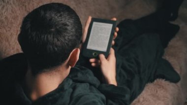 Bornozlu adam koltukta otururken e-kitap okuyor.