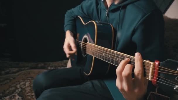 De mens speelt een akoestische gitaar terwijl hij op een bank zit — Stockvideo