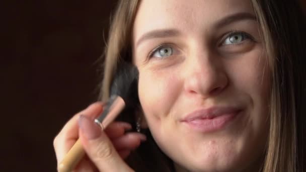 Rosto de uma bela jovem mulher aplicando blush com uma escova em seu rosto — Vídeo de Stock