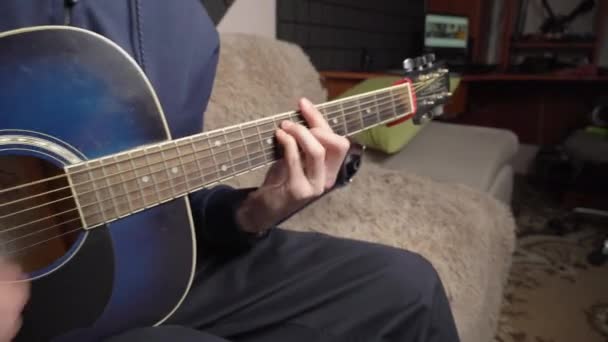 Человек играет на акустической гитаре, сидя на диване — стоковое видео
