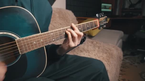 男はソファに座っている間にアコースティックギターを再生します — ストック動画